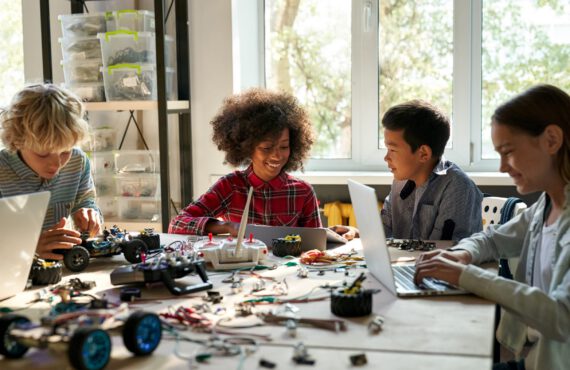 Group of multiethnic schoolkids interacting using gadgets for programming for robotics engineering class. Elementary school science classroom of futuristic technologies. STEM education concept.