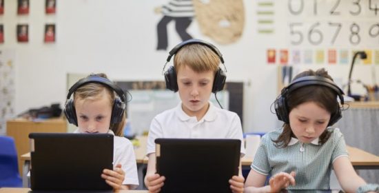 Schoolboy and girls listening to headphones in class at primary school