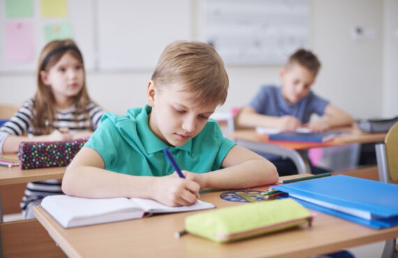 Schoolboy writing in exercise book in class